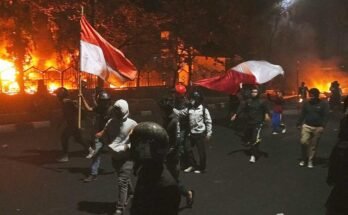 The demonstrators pass while the local building of the Parliament is engulfed in the flames during a demonstration after the death of a delivery rider in clashes between the riot police and the students protesting against the allowances of the legislators in Makassar, South Sulawesi, Indonesia, Friday August 29, 2025.